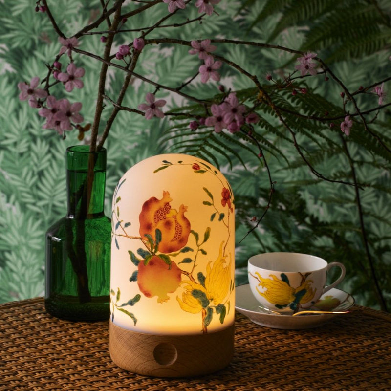 Decorative lamp with floral design on a table with a cup and saucer, vase, and cherry blossom branches.