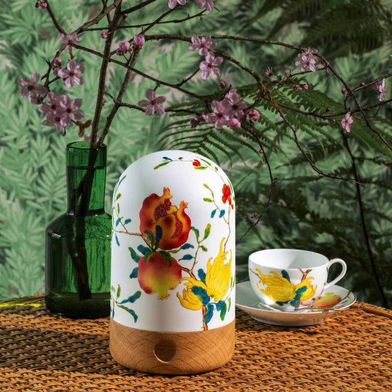Decorative lamp with floral design on a table with a cup and saucer, green vase, and cherry blossoms.