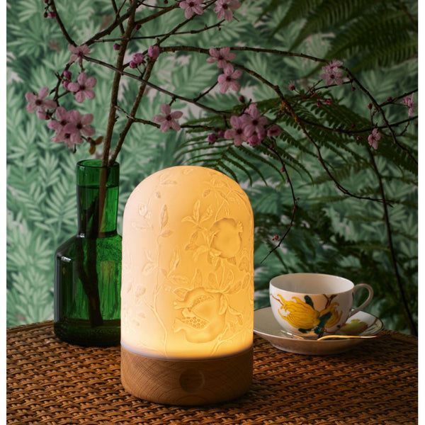 Decorative lamp on a table with a floral arrangement and teacup in the background