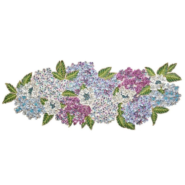 A decorative table runner featuring a floral pattern with hydrangea flowers in shades of blue, purple, and white, accented with green leaves.