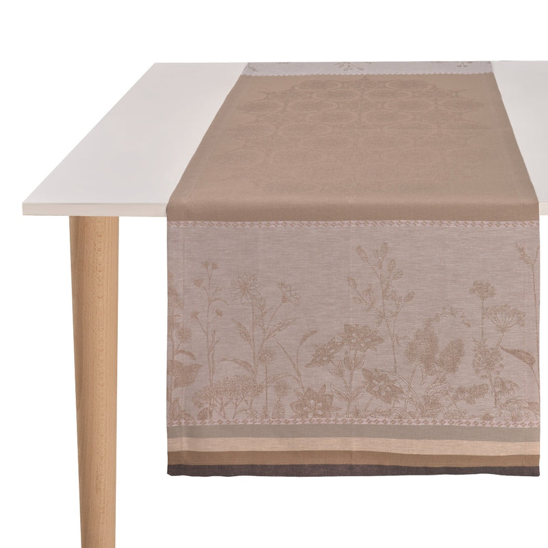 A beige linen table runner with a floral pattern, displayed on a white table.