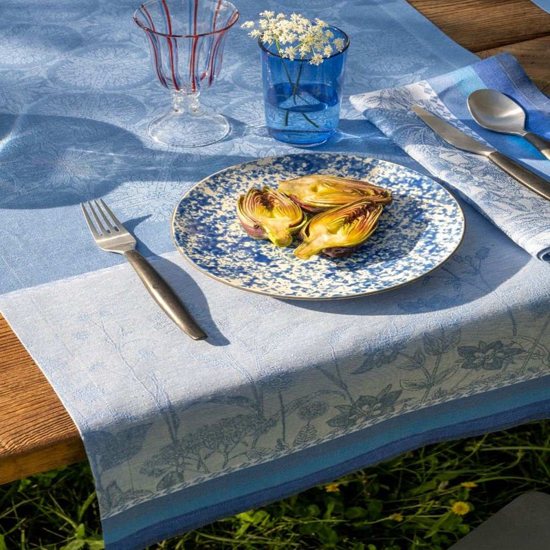 Table setting with a blue floral tablecloth, plate of artichokes, and cutlery outdoors.