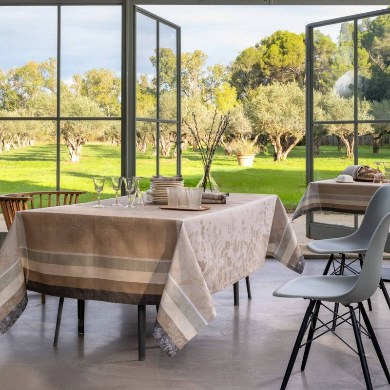 Dining area with striped tablecloth and chairs near large windows overlooking a garden.