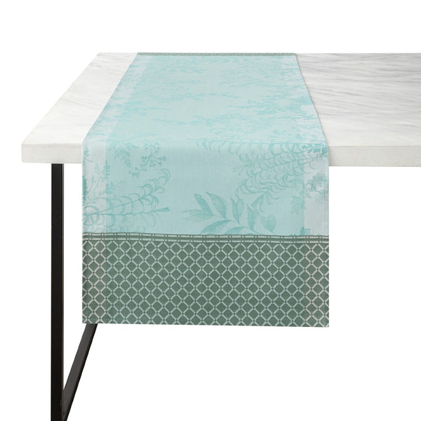 A blue and green floral patterned linen runner is displayed on a table, with part of a white tablecloth visible at the top.