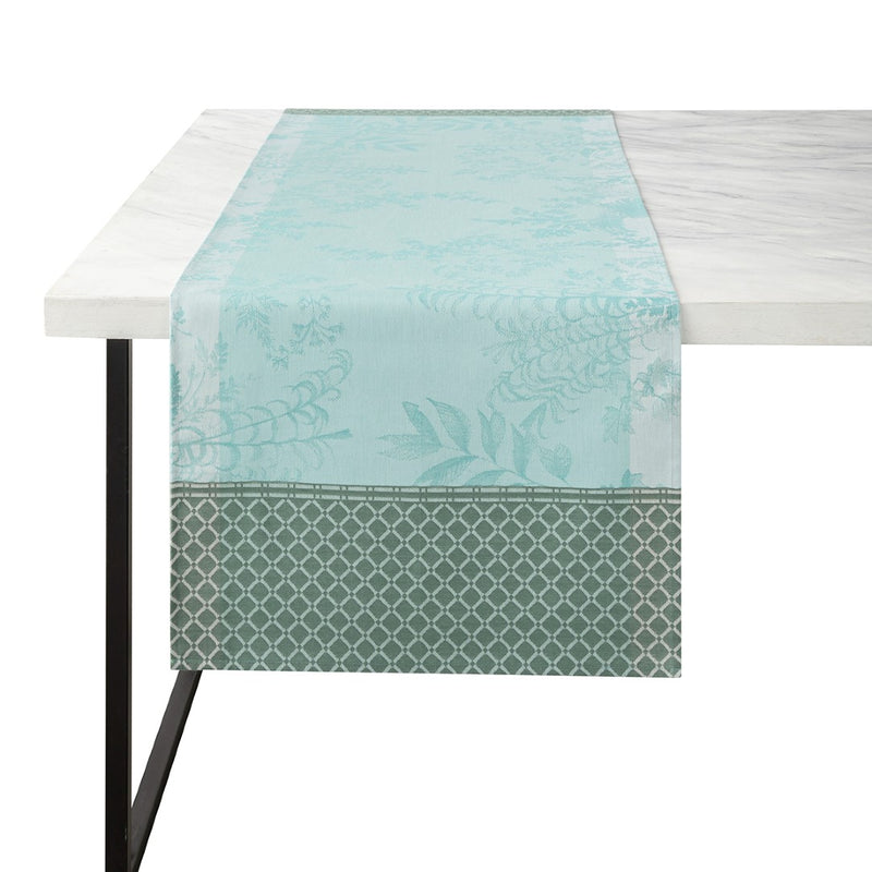 A blue and green floral patterned linen runner is displayed on a table, with part of a white tablecloth visible at the top.