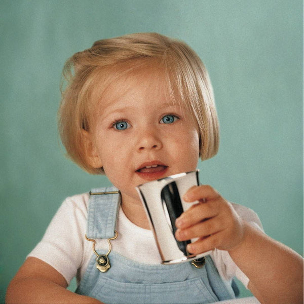 Child holding silver-plated baby cup with minimalist design by Ercuis against a green background