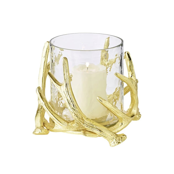A gold-colored candle holder with a clear glass bowl and decorative steel deer antlers supporting a candle.