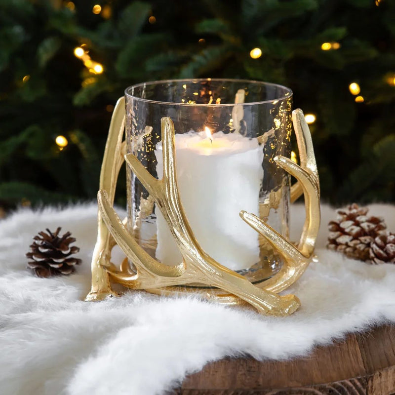 Gold antler candle holder with a lit candle on a snowy surface with Christmas tree in the background