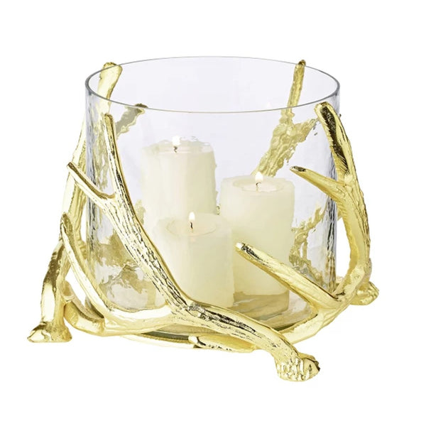 A clear glass candle holder with gold-colored steel deer antlers as a base, holding three candles.