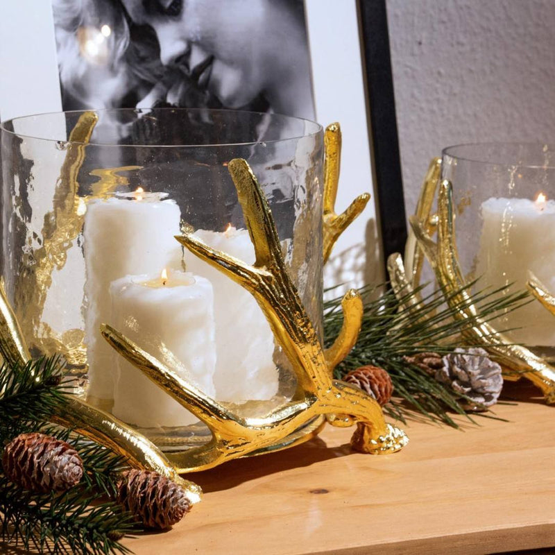Decorative candle holders with gold antler designs on a wooden surface.