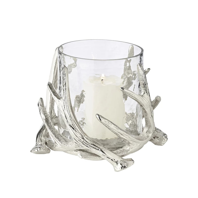 A silver candle holder with a clear glass bowl and decorative steel deer antlers supporting a candle.