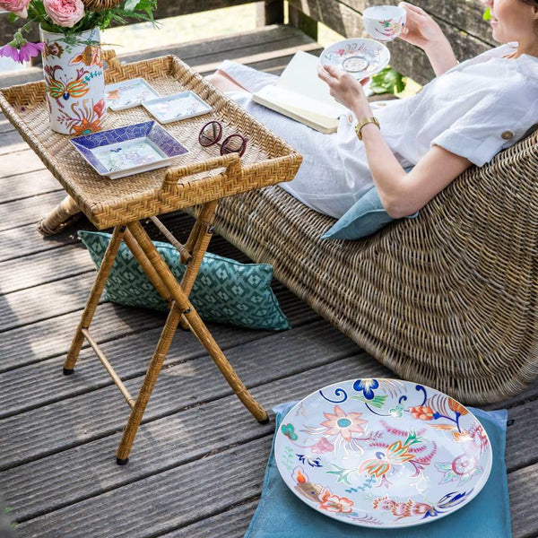 Person relaxing on a wicker chair with a tray of tea and Large Imari porcelain bowl on a wooden deck.