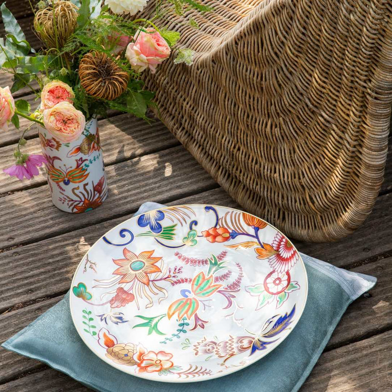 Decorative Large Imari porcelain bowl with floral patterns on a wooden surface with a vase of flowers and wicker basket.