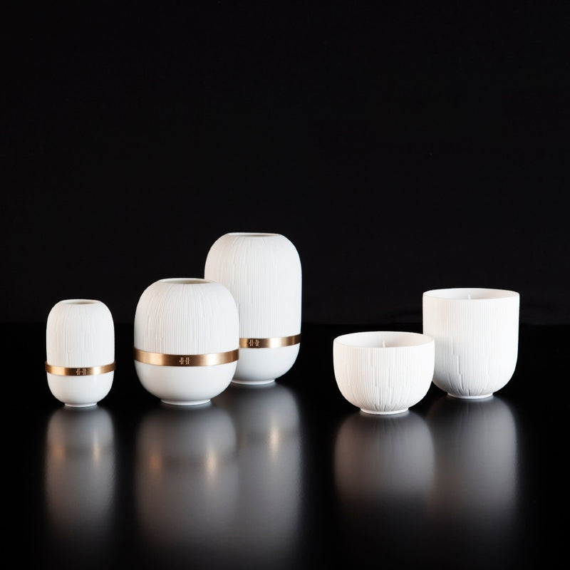 Set of white ceramic candle holders with gold bands on a black background