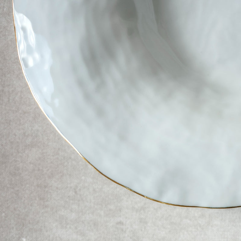 Close-up of a Set of 2 large deep plates white with golden rim No7 Indulge porcelain on a textured beige surface