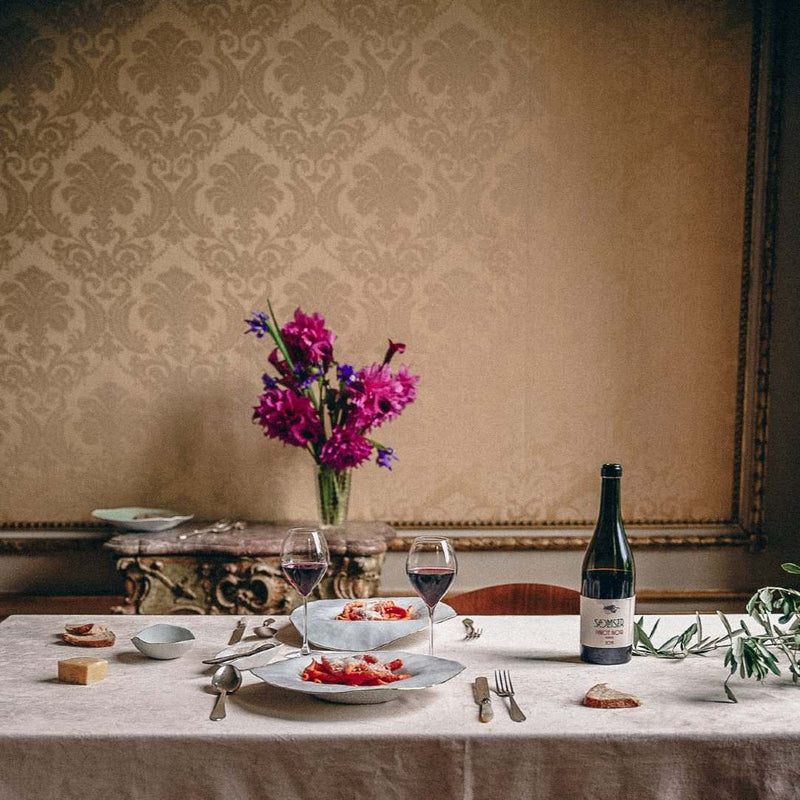 Dining table set with Set of 2 large deep plates white with golden rim No7 Indulge porcelain, wine glasses, and a bottle of wine against a decorative wall.