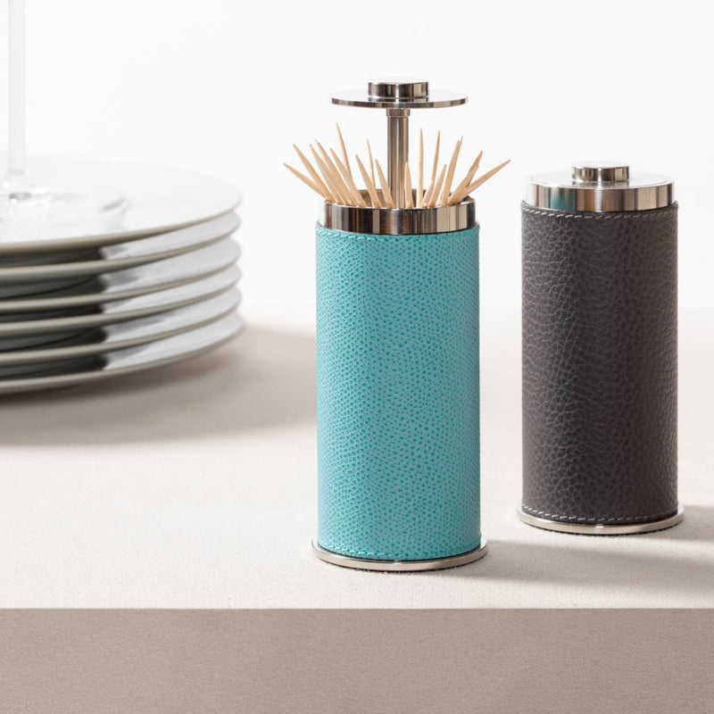 Two toothpick holders Otello containers with textured leather exteriors and metal tops on a light surface.