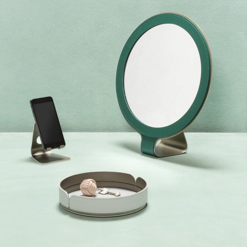 Round mirror with green frame, phone stand, and jewelry dish on a light green background