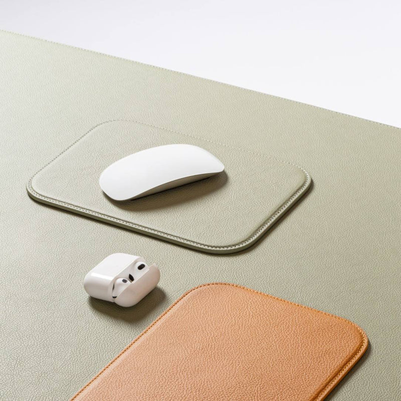 White mouse and wireless earbuds on a green mouse pad with a brown leather sleeve.