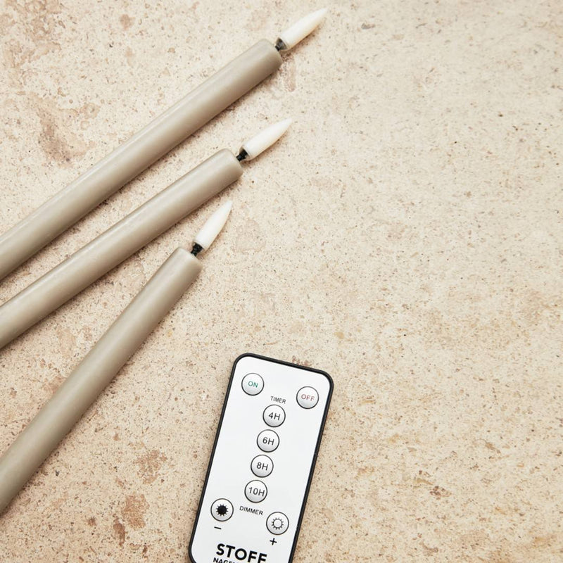 led stoff Three beige candles and a remote control on a textured surface