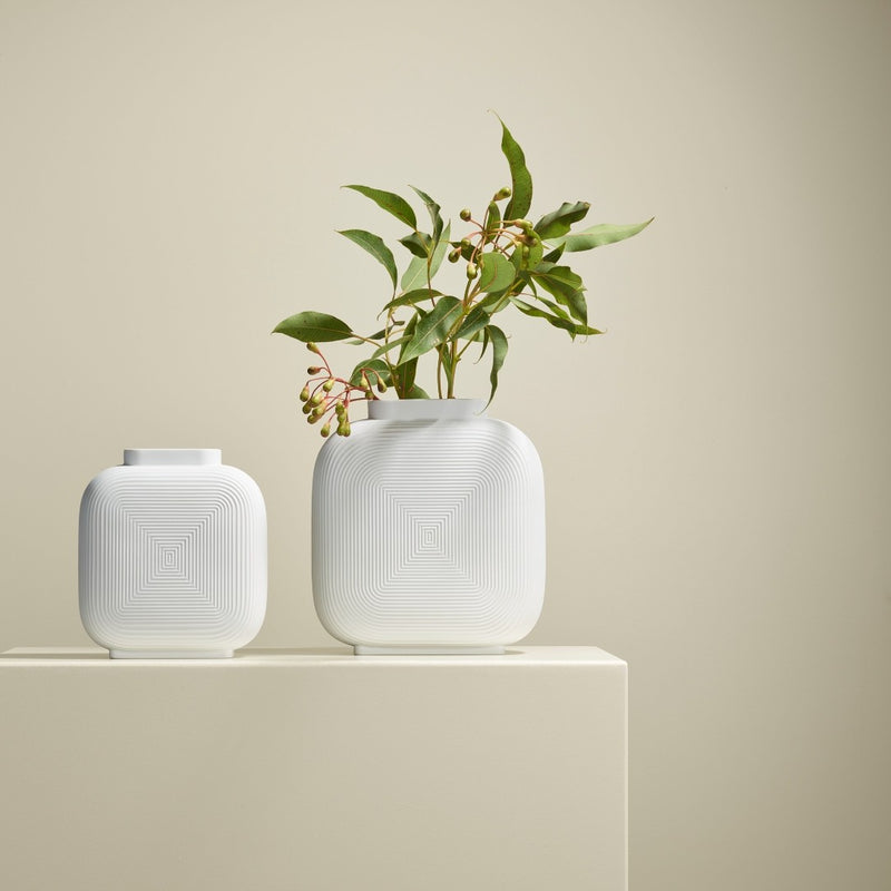 Two white textured vases with a plant on a beige surface and background