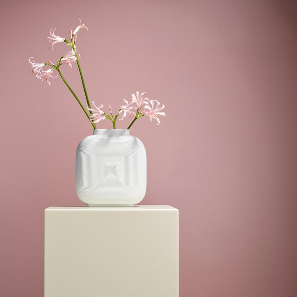 White textured vase with pink flowers on a light beige pedestal against a pinkish-purple background