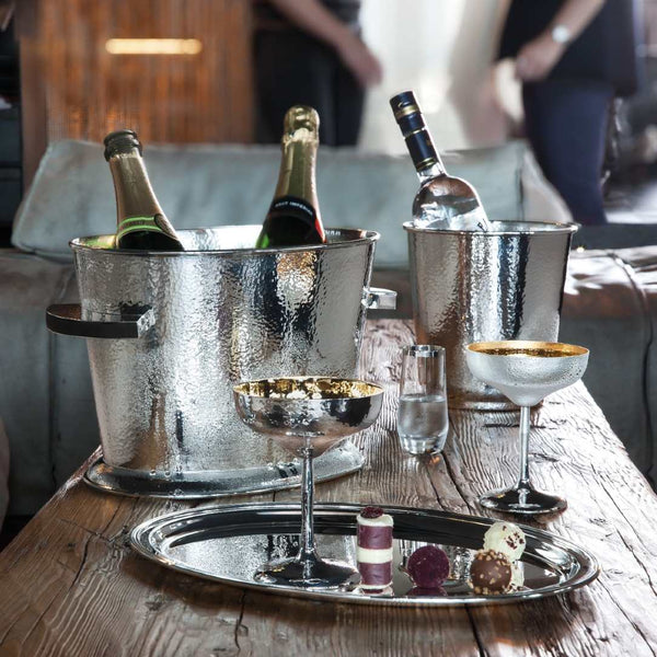 Bottles of champagne in ice buckets with Crystal Liqueur Glass with Hand-Applied Silver Rim – Avantgarde by Sonja Quandt on a wooden table.