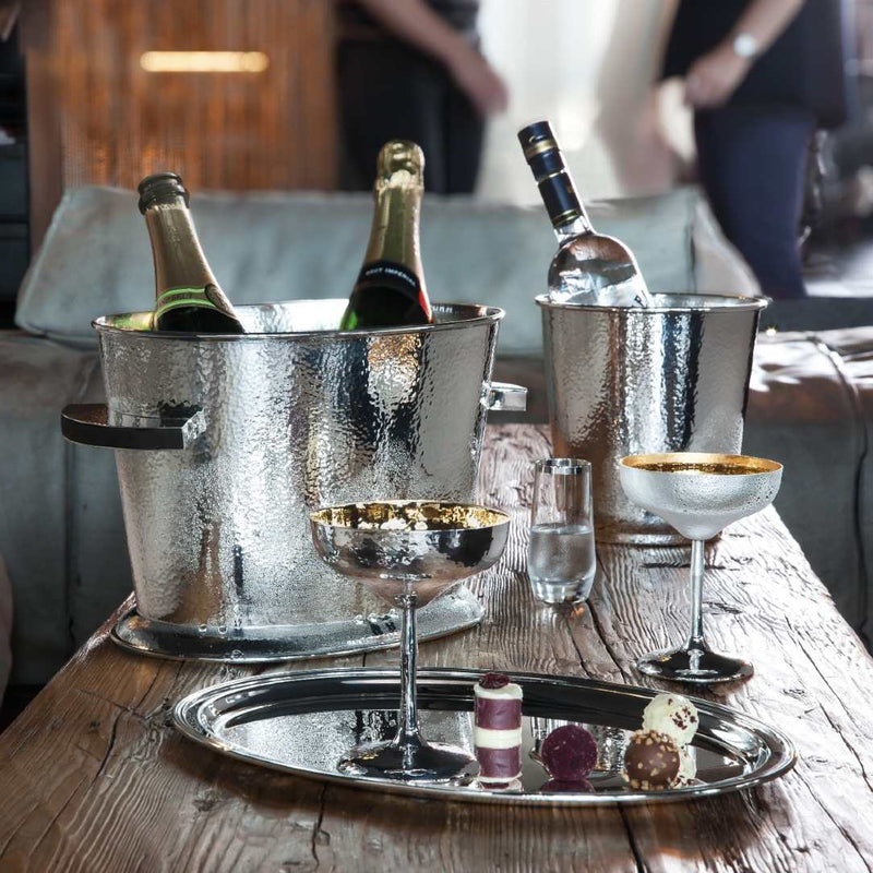 Bottles of champagne in ice buckets with Crystal Liqueur Glass with Hand-Applied Silver Rim – Avantgarde by Sonja Quandt on a wooden table.