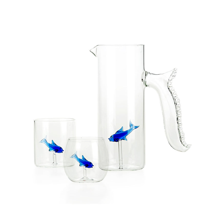 Clear glass pitcher and tumblers with blue fish designs on a white background