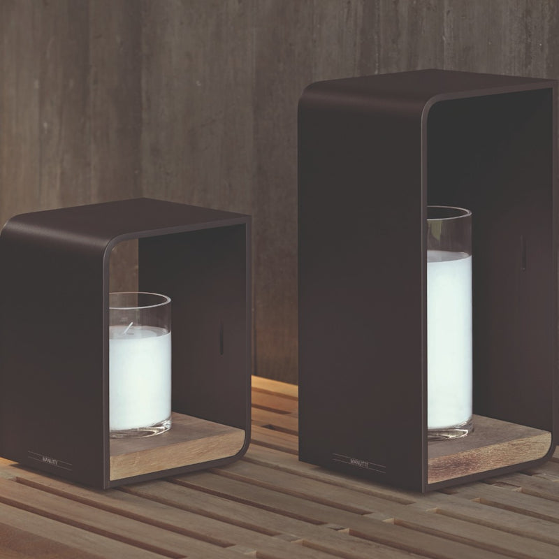 Two modern candle holders with candles on a wooden surface.