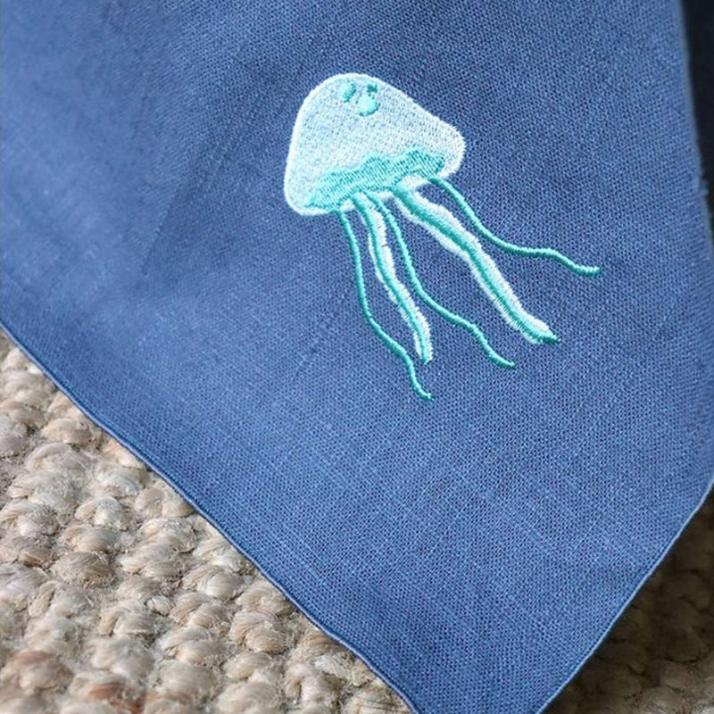 Blue fabric with a teal embroidered jellyfish design on a textured surface