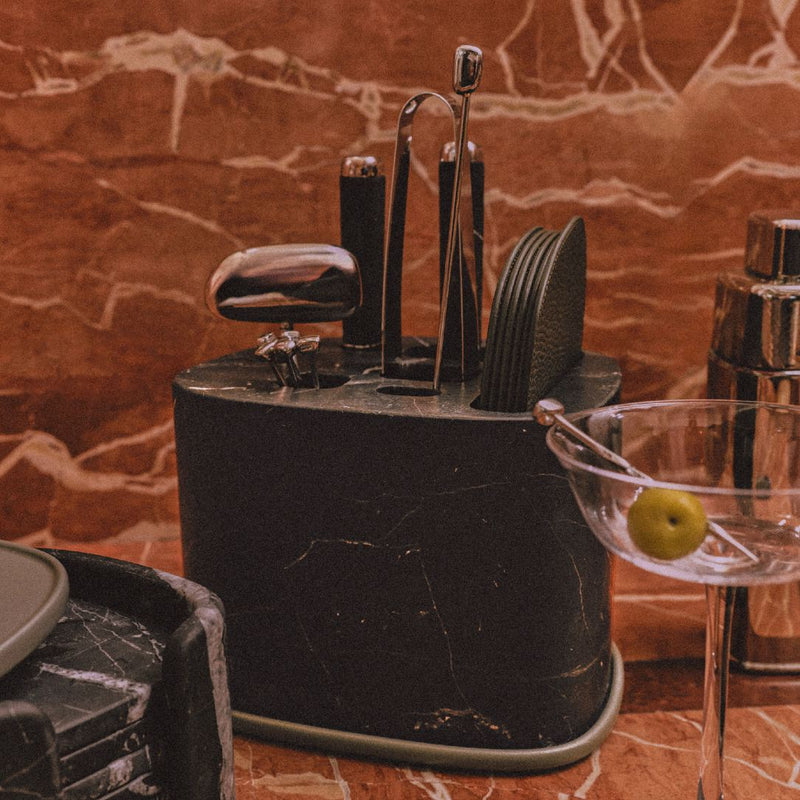 Close-up of the Maris bar accessories set by Kelly Wearstler x Giobagnara with marble base in black, stainless steel tools, and leather coasters