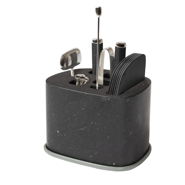 A black marble bar accessory holder with sandblasted aluminium accents, containing an assortment of stainless steel bar tools, including a corkscrew, cocktail picks, bottle opener, knife, ice tongs, and a mixing spoon.
