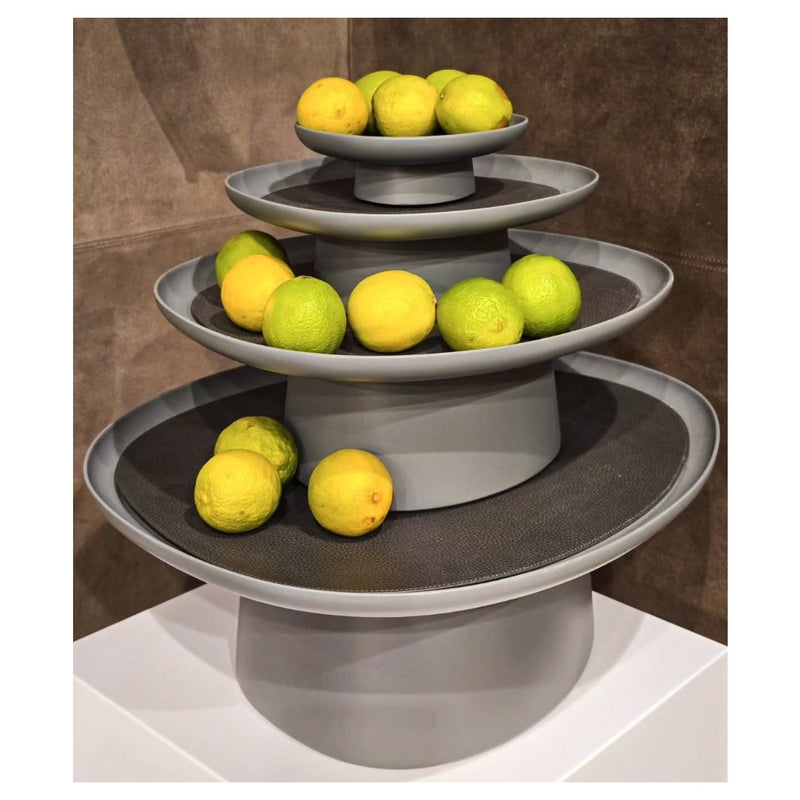 Three-tiered gray fruit stand with lemons and limes on a neutral background