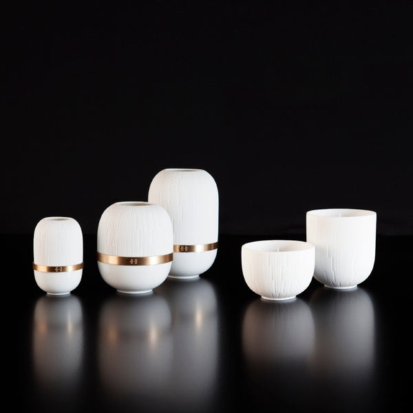 Set of white ceramic candle holders with gold bands on a black background