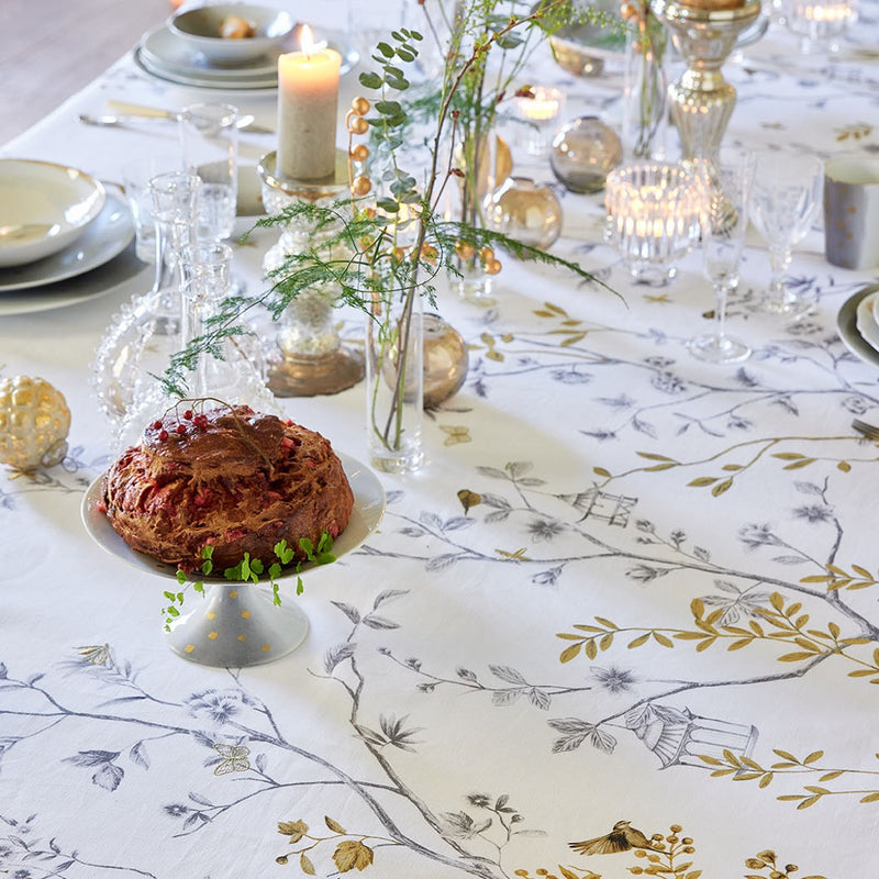 Close-up White linen tablecloth with bird and trees embroidery on a table with a cake, plates, glassware and candles