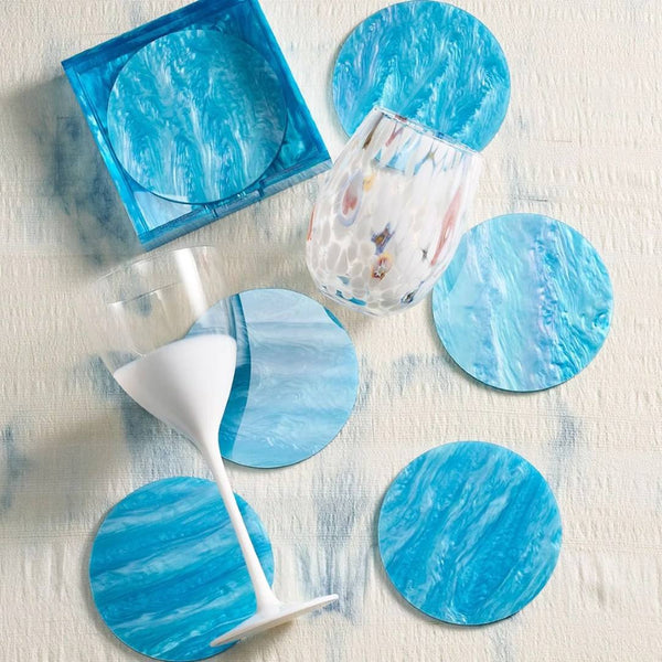 Set of blue marbled coasters on a light wooden surface with a glass and napkin.