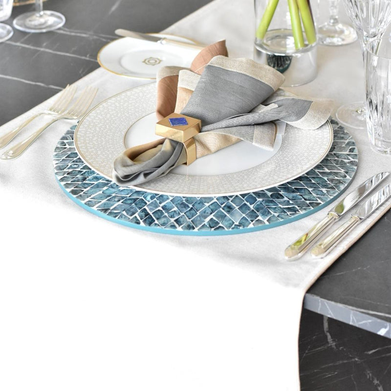 Dining table setting with a decorative placemat, plates, and cutlery on a marble surface.