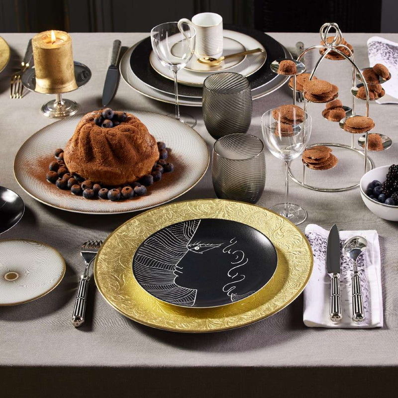 Elegant table setting with gold and black plates, desserts, and glasses.