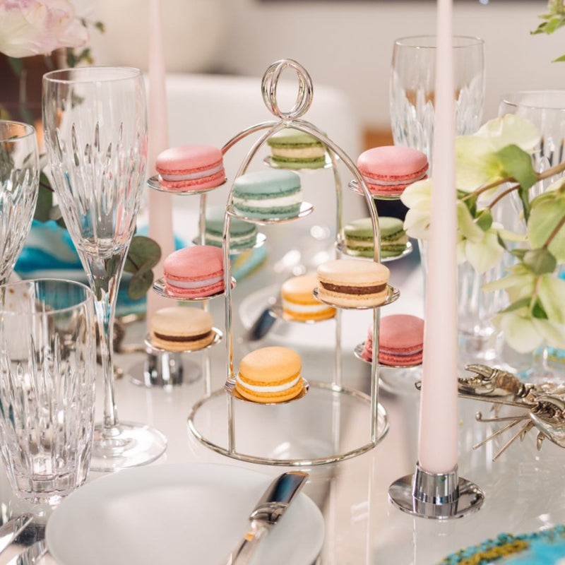 Decorative table setting with macarons on a stand, glasses, and flowers.
