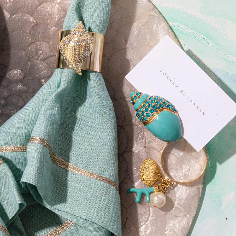 Decorative napkin ring with turquoise and gold design on a teal napkin and stone surface.