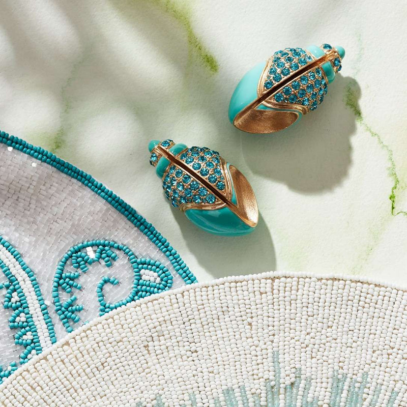 Turquoise and gold place card holders on a textured white surface with green leaves.