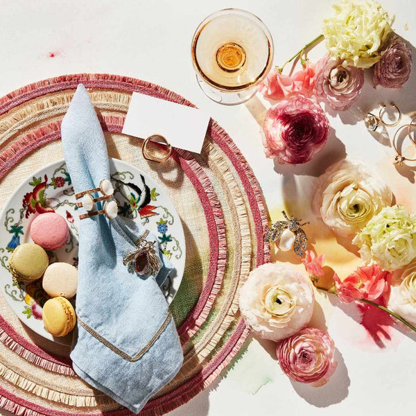 Decorative table setting with flowers, macarons, Knot Place Card Holders in Worned Gold Zinc by Joanna Buchanan on a white surface.