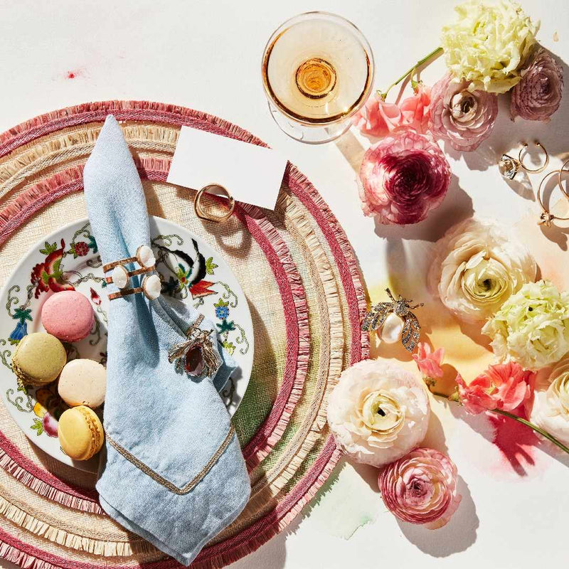 Decorative table setting with flowers, macarons, Knot Place Card Holders in Worned Gold Zinc by Joanna Buchanan on a white surface.