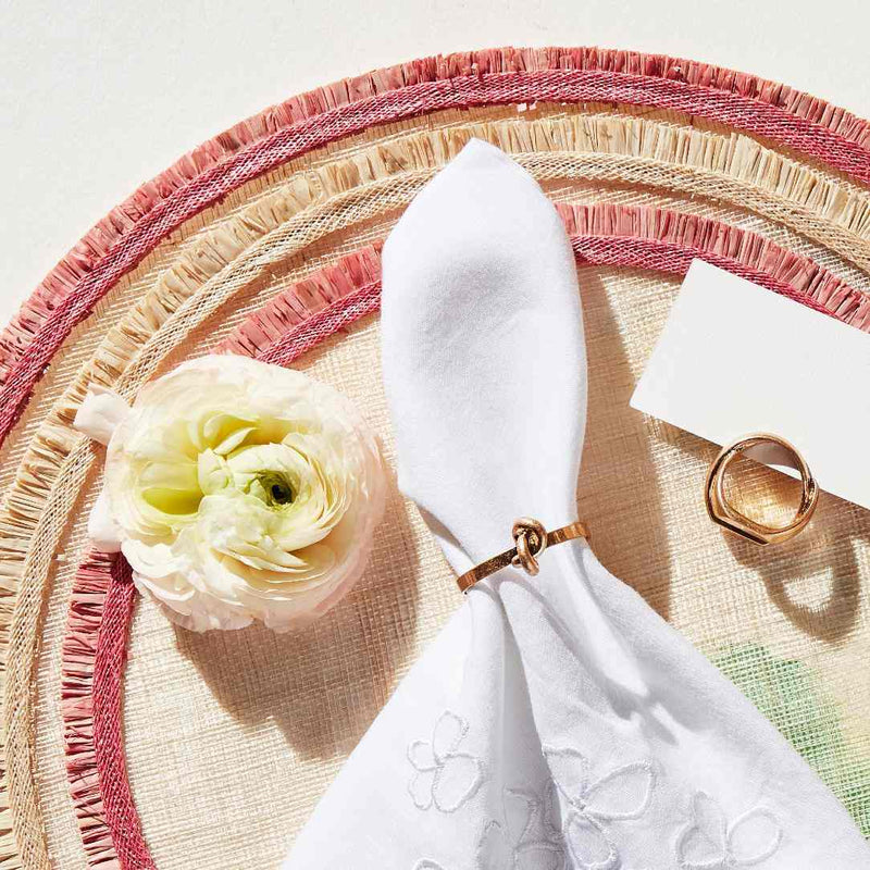 Decorative table setting with a white flower, Knot Place Card Holder by Joanna Buchanan, and white napkin on a woven placemat.