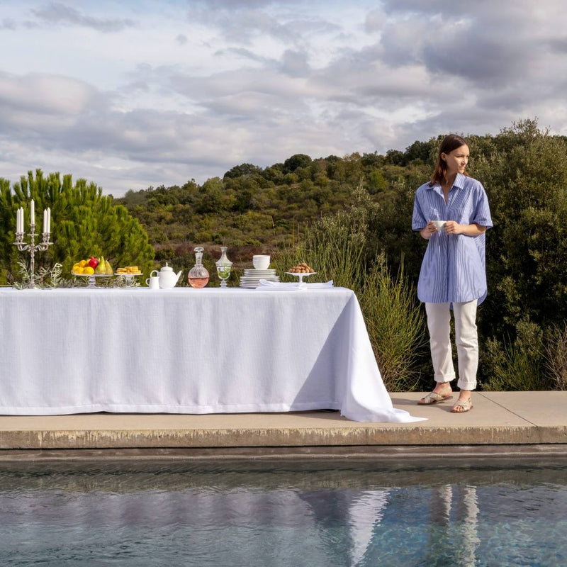 Woman standing by a table set outdoors by a pool with a scenic background