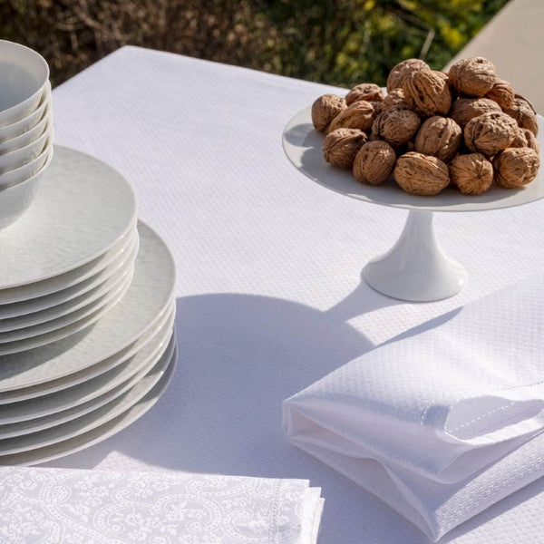 Stack of white plates on a white tablecloth with a bowl of walnuts.