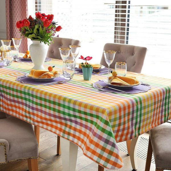 Dining table set with a colorful checkered tablecloth, plates, glasses, and flowers.