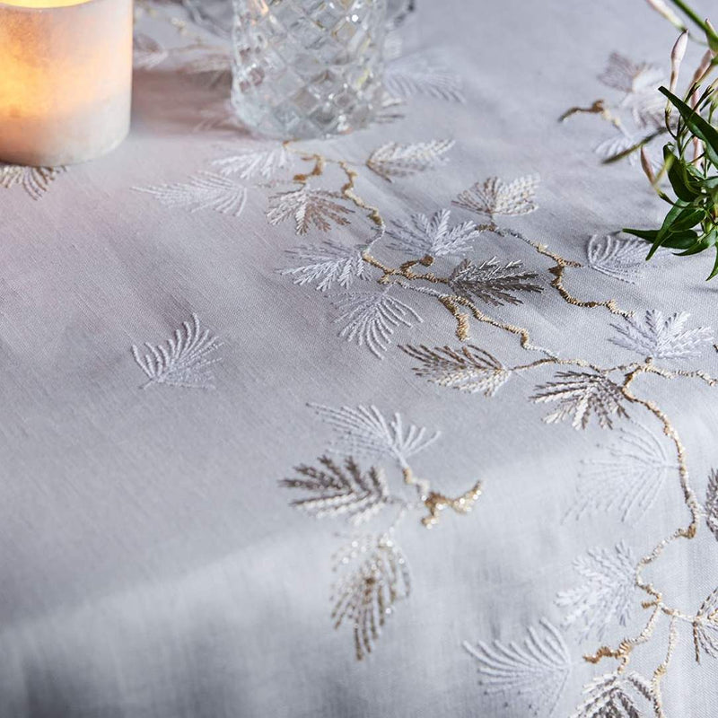 Embroidered tablecloth with gold and silver designs on a white tablecloth.