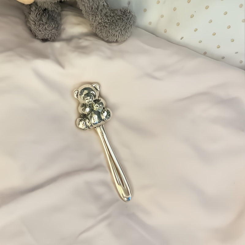 Silver teddy bear-shaped rattle on a soft surface